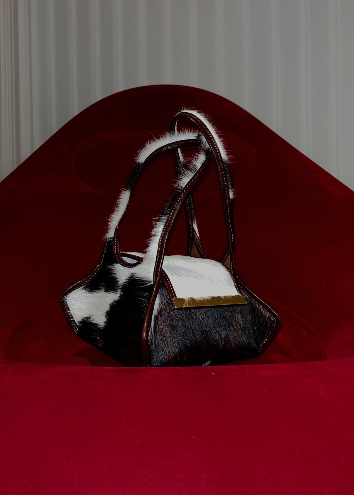 The Swing Leather Bag in Color Pony Hair with Gold Hardware on a red blow up couch