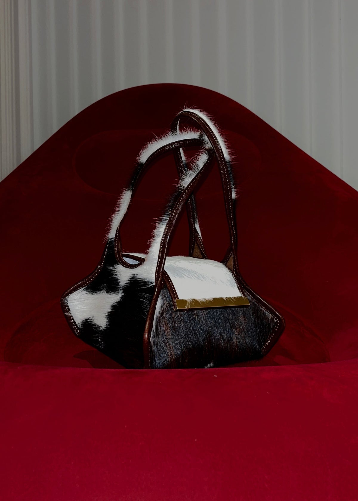 The Swing Leather Bag in Color Pony Hair with Gold Hardware on a red blow up couch