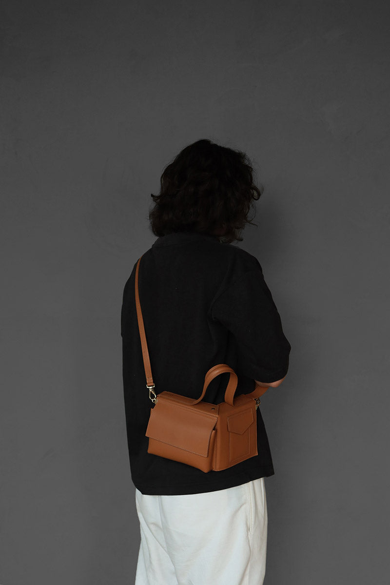 A Male Model carrying the corner guard leather cross shoulder bag in color Tan