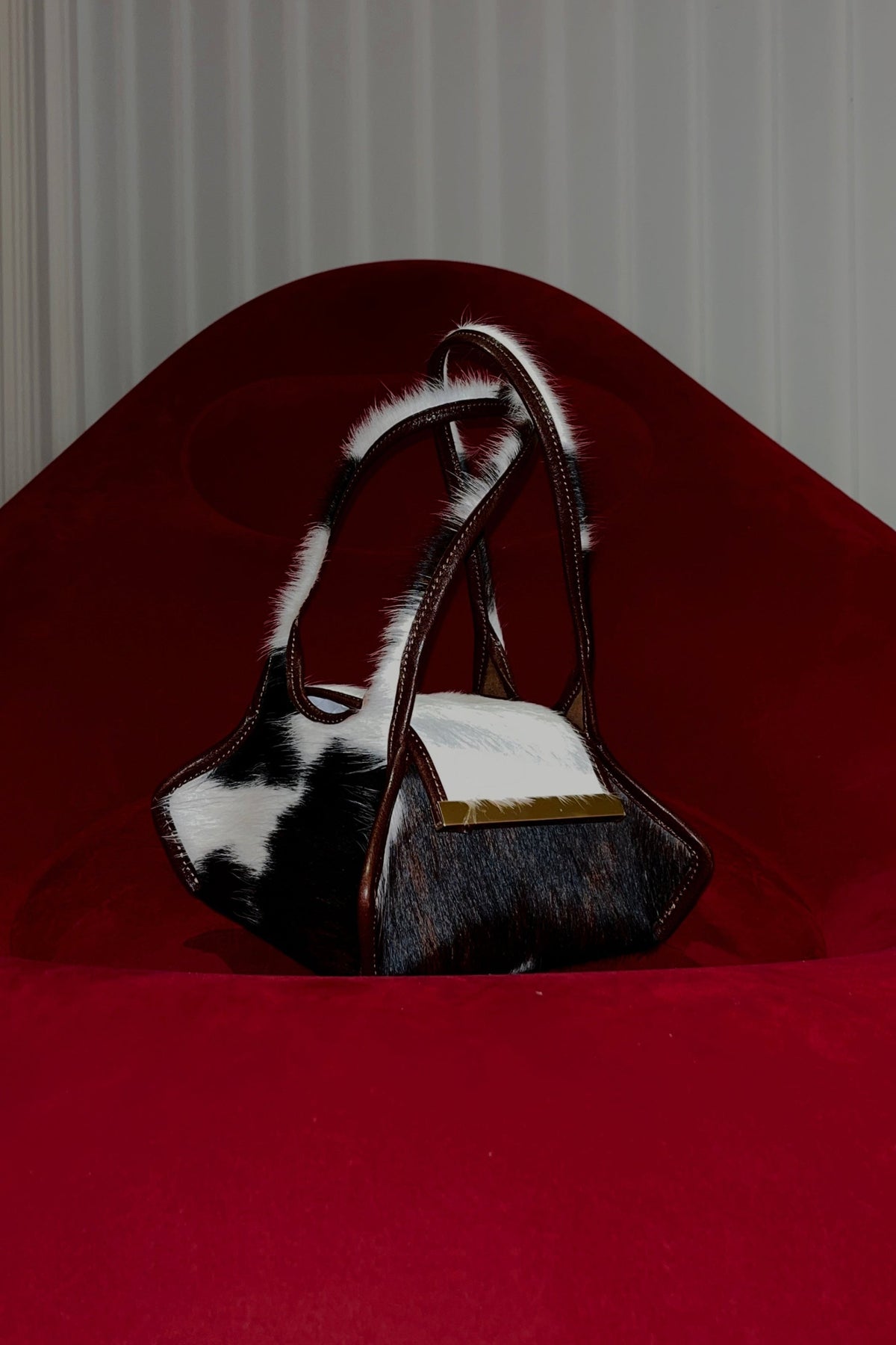 The Swing Leather Bag in Color Pony Hair with Gold Hardware on a red blow up couch