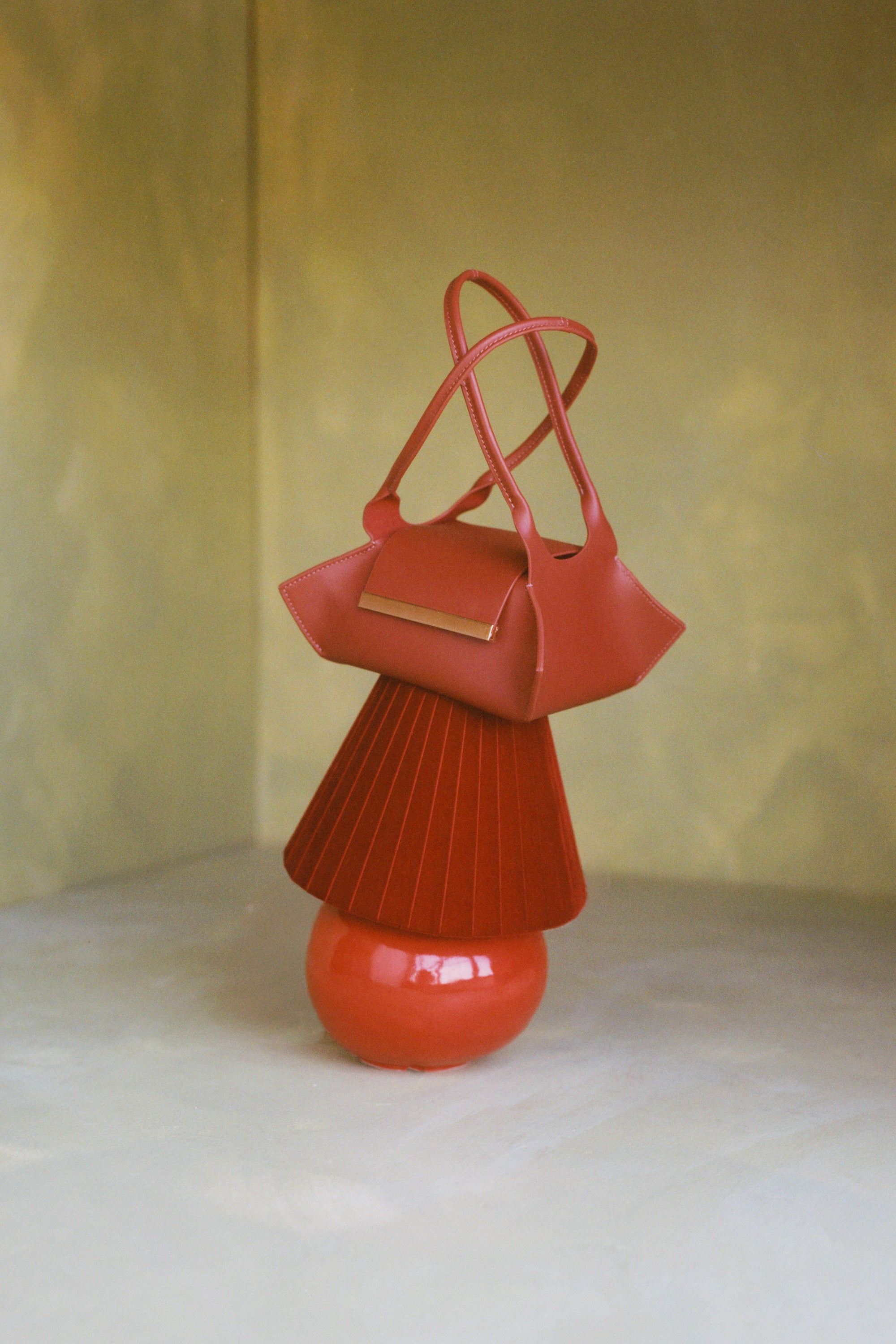 The Swing Leather Handbag in color Rust in a green set with sitting on a red lamp