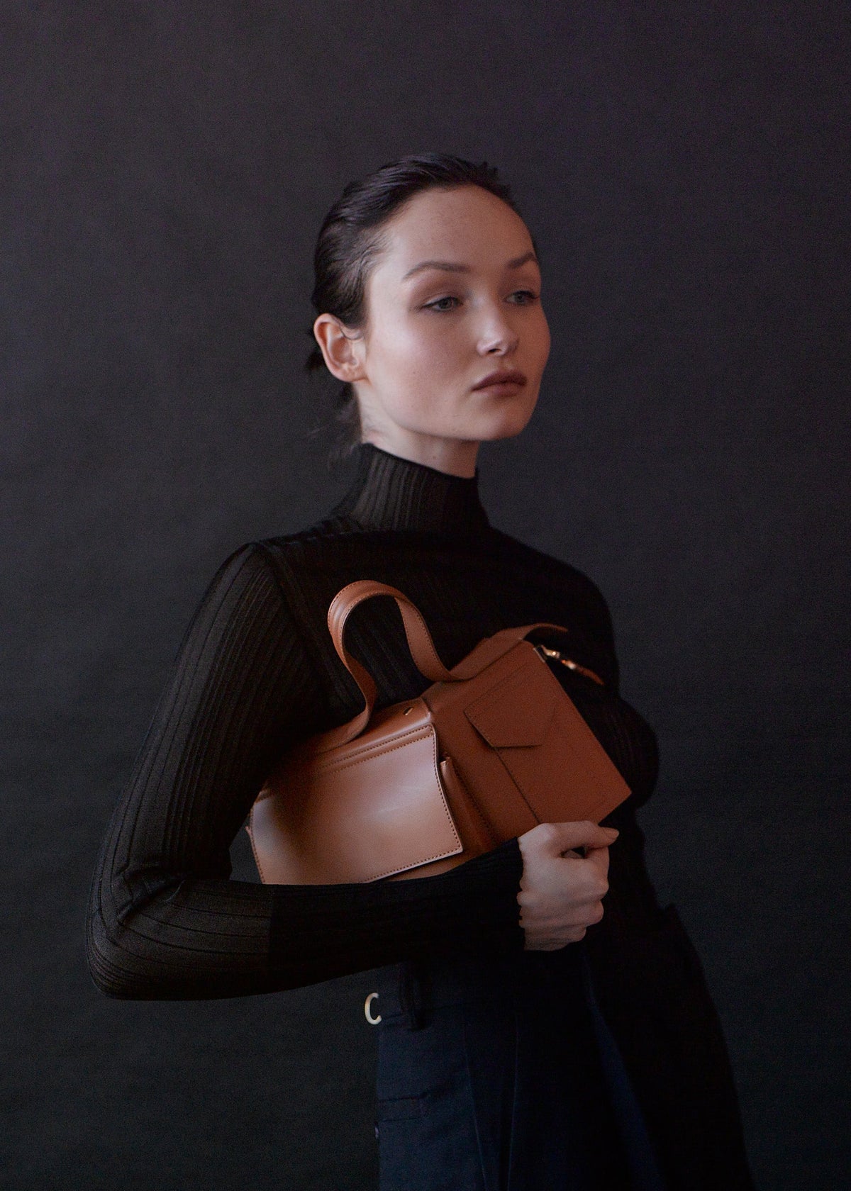 A model carrying The Corner Guard Leather Handbag in color Tan.