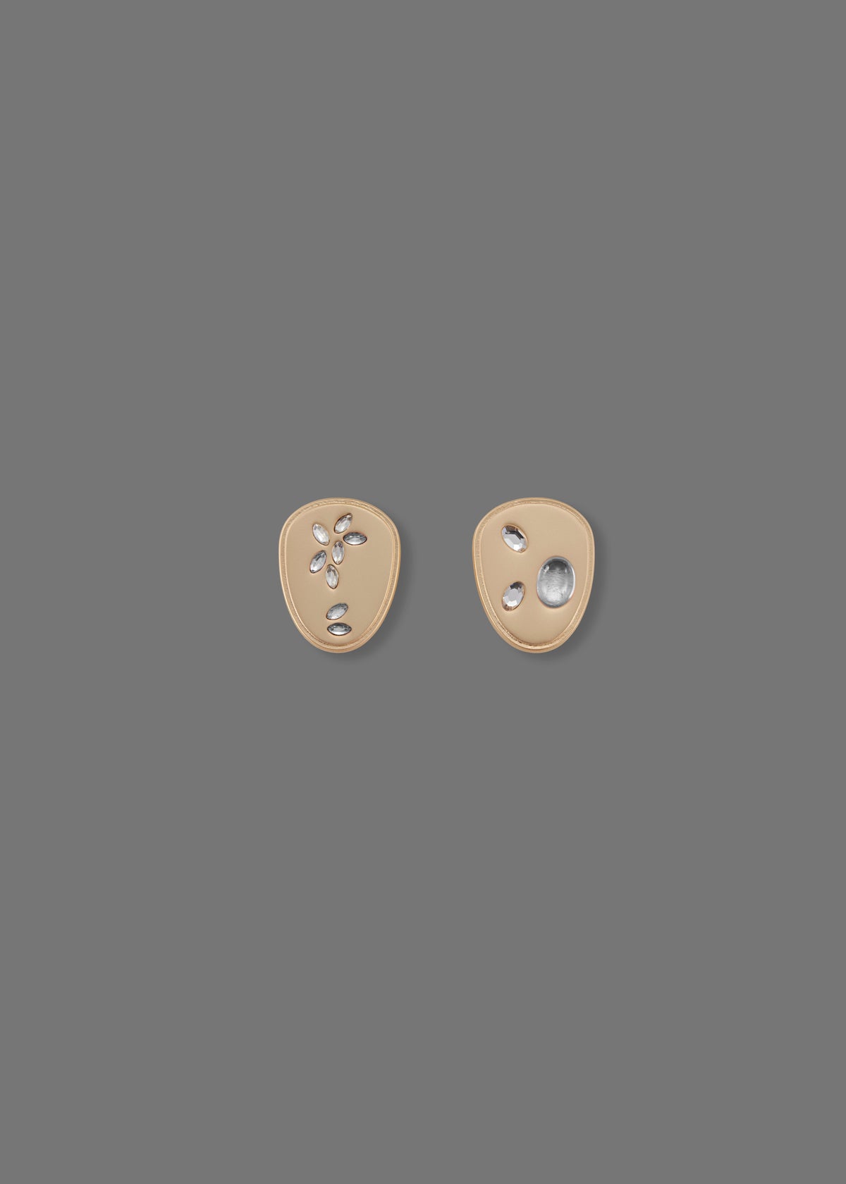 The Seed Earring: Gold-plated asymmetrical earrings with cabochon crystals — in clear — embedded on a flat surface.